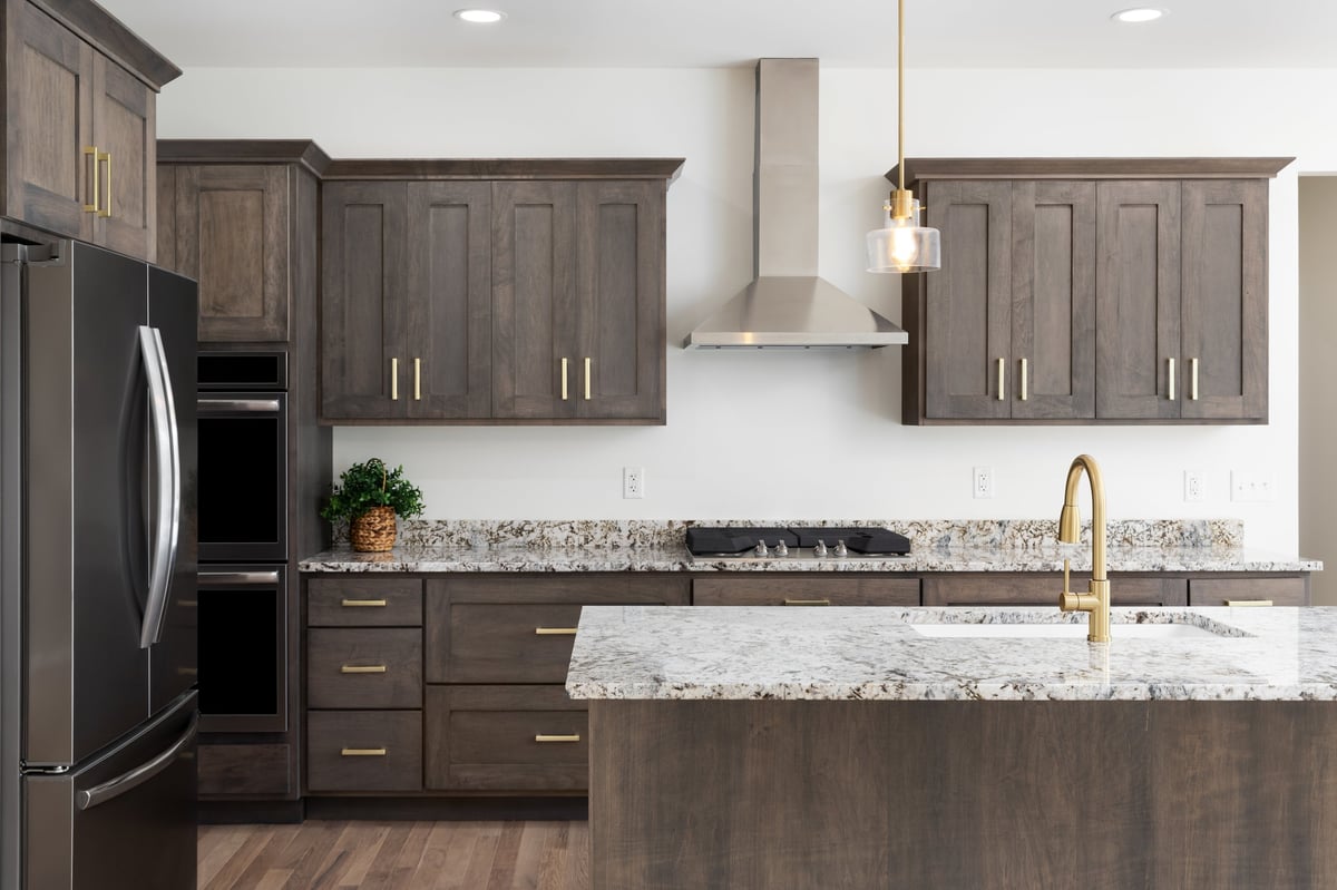 Luxury kitchen featuring dark wood custom cabinetry, gold pendant lights, granite countertops, and premium stainless steel appliances